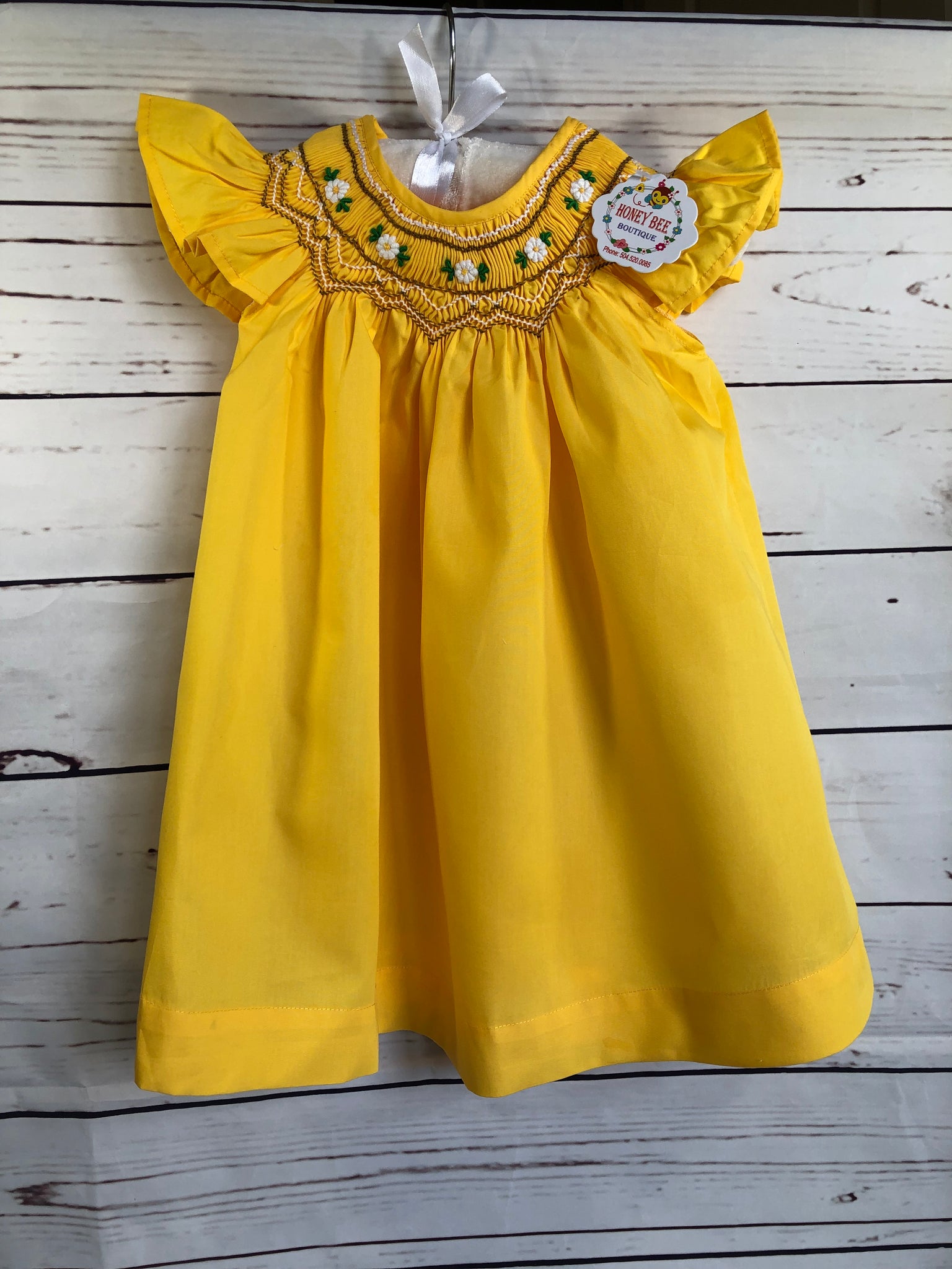 Bright yellow dress with white flowers and brown smocked details